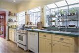 The dining room flows into the the kitchen, which mixes colorful cabinetry and tile counters with vintage-style appliances. A series of greenhouse windows were added along the wall.