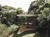 Outdoor, Trees, Grass, Side Yard, Walkways, and Shrubs To ensure structural integrity, the architects designed the home’s living spaces to be perpendicular to the sloping topography, and the roofline to be in harmony with the ground level, canopy, and horizon.  Photos from Budget Breakdown: This Ethereal Glass House in the Brazilian Forest Was Built for $187K
