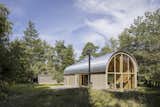 Situated in a small forest clearing near the Kattegat seashore in Denmark, Vibo Tværveh interprets a barrel-vault structure through traditional Danish cabin and barn architecture. The team topped the tube-shaped structure with industrial steel plates, and they clad the majority of the interior in pine. "We wanted the smell, sound, and atmosphere of the residence to embody a traditional cabin," says architect Stefan Valbæk. He describes the long, barrel shape of the house as "simple, yet notable," and says that inside, the high ceiling and "distinctive rhythm" of the arched steel beams create "an extraordinary spatial atmosphere" with "views to the treetops and the sky."&nbsp;