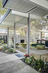 Outside, deep overhangs provide shade for the glass-walled living area. Lush new landscaping borders the patio and facade.