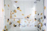 The shower is clad with a playful, abstract array of white, gold, and black tiles.