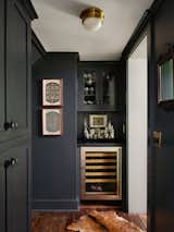 Previously, this quirky space had a pantry, broom closet, and doors leading to the basement. Now, this niche houses a butler's pantry with a custom dry bar, wine fridge, and storage cabinets awash in Farrow &amp; Ball Studio Green with a Soapstone countertop.