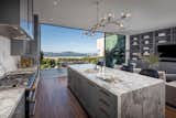 The kitchen features a striking marble island and top-of-the-line appliances. Expansive Vitrocsa sliding doors open to one of the home's many terraces.