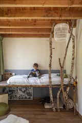 Nine-year-old Stan reads on the platform bed his father built for him. A trio of birch branches helps to bring the outdoors in. The pendant and bed linens are custom.