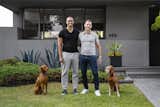 Outdoor, Front Yard, Grass, Raised Planters, Shrubs, and Walkways Residents Silas Munro and Bill Hildebrand stand outside their home with their two Viszlas, Niko and Jordy.  Photos from A Trio of Schindler Houses Brings Together Three Design-Minded Los Angeles Families