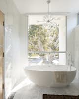 The second-floor bathroom features a freestanding tub and more marble cladding. A floor-to-ceiling window frames another view of the prominent fig trees.