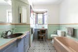 One of the bathrooms features contrasting shades of pastel-colored tiles and paint. A small make-up area is nestled below a bay window, while a copper sink completes the vanity.