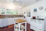 A series of windows run above a tiled countertop and backsplash in the kitchen. A vintage stove sits along another wall.