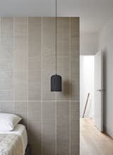 In the couple's bedroom, a Gap pendant from Woud hangs in front of a wall clad in STI Otto porcelain tile from Stone Tile.