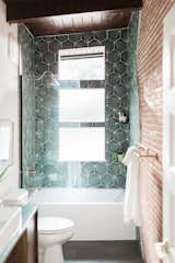 Now basking in natural light, the renovated bathroom offers all-new finishes, including brightly colored tiles that contrast with the exposed brick wall.
