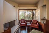 The penthouse's main bedroom features a large fireplace, mahogany-paneled walls, and a large window overlooking the treetops.  Photo 9 of 14 in A Newly Restored Schindler Building Lists for $3.65M in L.A.