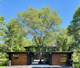 Recently listed in Bayside, Wisconsin, this renovated midcentury property comprises two detached structures—a two-bay garage and a barrel-vaulted house—connected by a central patio. A pass-through between the garages is punctuated by a large tree growing in the middle.