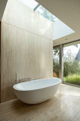 The skylight and floor-to-ceiling glass windows invite nature into the bathing area of the bathroom.