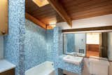 The first of two full bathrooms features a skylight over the tub and vanity, both of which are clad in a mosaic of blue tile. An original set of cabinetry provides additional storage in the corner.
