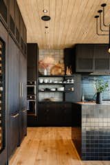 The kitchen features oak cabinets stained in a dark grey and navy tile from Heath Ceramics. These darker elements are balanced by the tongue-and-groove wood ceiling and floors, as well as ample sunlight entering through the steel-framed glass doors.