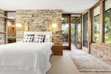 Located at the end of a long hallway of bedrooms, the principal suite features walls clad in stacked stone and brick, along with numerous windows overlooking the surrounding treetops.