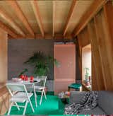Inside the flat, a bright green resin floor (which is also heated) spans throughout, contrasting against the neutral-toned wood and cement walls. A light pink perforated storage cabinet adds another pop of color to the space.