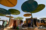 While much of rural African life revolves around weekly trading gatherings, the economy of individual villages can barely survive. Atelier Masomi hopes to change this with a design that could, if emulated across the region, give communities in an arid landscape short on natural resources a much-needed economic boost and a sense of pride. The architecture firm built a permanent regional market in the village of Dandji with canopies made of cheap and recycled materials that now operates daily instead of weekly. Adapting the regions’s traditional market typology of adobe posts and reed roofs, the design uses compressed earth bricks and metal in a durable, quirky, and visually striking manner. It is also incredibly practical. Colorful, recycled metal disks provide shade usually cast by trees in less severe climates, while arranging them at different levels ensures good ventilation. The compressed earth bricks used for the stalls have similar cooling advantages of the more traditional adobe, but at a fraction of the cost. Bringing this dramatic upgrade to the village infrastructure full circle, the site is centered around an ancestral tree with landscaping that encourages newcomers to gather and sit with the local villagers, increasing interaction socially as well as economically.