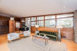 Another view of the living area shows the wall of windows at the front facade. The adjacent stairs lead up to several bedrooms, and down to the kitchen/dining area.