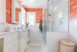 The connected bath is fitted with vibrantly colored wallpaper, a marble countertop and sink, along with penny-tile floors.