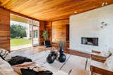 In another gathering area, a broad concrete fireplace contrasts the warmth of the wooden ceiling, floor, and walls. An oversized picture window floods the space with natural light.