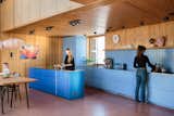The main kitchen, where Margit, left, is working with her niece Sarah, has a bright blue island that offers a striking contrast to the warm-toned wood and pink floors. “We wanted a color that would transform it into an object that really stands out in the room,” says Thurmann-Moe. “It’s almost like a sapphire.”