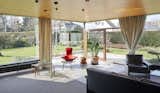 Floor-to-ceiling glazing frames much of the living room, presenting an intimate connection with the home's green surrounding. A wood-framed glass door offers direct outdoor access.  Photo 6 of 13 in A ’60s Time Capsule by Belgian Brutalist Juliaan Lampens Lists for €545K