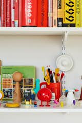 A wall of shelves holds color-blocked books, 3D-printed prototypes (including several versions of Joshua’s soy sauce cruet), and objets the designer has collected over the years, like a 1937 Top-O-Stove Potato Baker by Raymond Barton and salt and pepper shakers by William Lescaze.  Photo 7 of 18 in Rental Revamp: A Brooklyn Designer Proves That 88 Square Feet Don’t Have to Feel Small