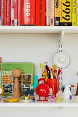 A wall of shelves holds color-blocked books, 3D-printed prototypes (including several versions of Joshua’s soy sauce cruet), and objets the designer has collected over the years, like a 1937 Top-O-Stove Potato Baker by Raymond Barton and salt and pepper shakers by William Lescaze.  Photo 5 of 18 in Rental Revamp: A Brooklyn Designer Proves That 88 Square Feet Don’t Have to Feel Small