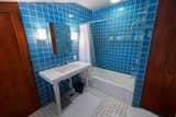 Bold blue tiles stretch across the walls in a bathroom located off a long, narrow corridor.
