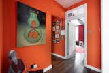 Original hardwoods line the bright-orange hallway, which serves as another gallery for art.