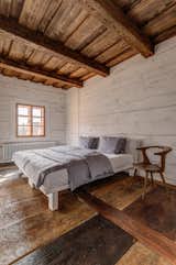 The bedroom on the main level is fitted with wide-plank floorboards, whitewashed walls, and exposed beam ceilings, which presents a similar aesthetic to the primary living spaces.
