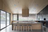 Kitchen, Wood, Wood, Ceiling, Pendant, Range Hood, Concrete, and Cooktops  Kitchen Ceiling Pendant Concrete Range Hood Wood Photos from A Cathedral-Esque Lake Home Rises in the Quebec Countryside
