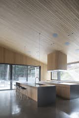 Kitchen, Range Hood, Wood Counter, Wood Cabinet, Concrete Floor, Pendant Lighting, and Ceiling Lighting  Photo 3 of 17 in A Cathedral-Esque Lake Home Rises in the Quebec Countryside