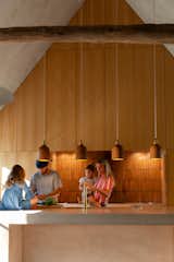 The family gathers in the kitchen, which features oak cabinets, a concrete island, and brass fixtures. The backsplash is made of pink bricks hand-selected by Alix and Onur from a nearby brickyard. The mango wood pendants were purchased in a market in Bangkok.&nbsp;