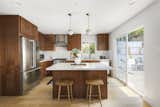 Rich wooden elements continue into the kitchen, contrasting with the white tiled backsplash and stainless steel appliances. Designer pendant lighting gracefully hangs over the central island.