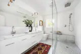 The connected bath features an oversize glass shower and a long, double-sink vanity.