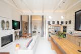 Another view of the main living areas showcases the soaring, vaulted ceilings, along with the two circular windows above the kitchen, which draw in additional light. Slender white columns subtly divide the spaces from the small entry lounge and private wing beyond.