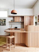 This 1890s home in Melbourne, Australia, received a ground-level renovation with custom joinery made of recycled wood. A curved kitchen island features a concealed bar and a wooden ladder attached to a brass rail that provides access to the ceiling-height Laminex storage cupboards.