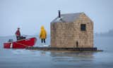 A motorboat tows the sauna out into the harbor. The structure is covered in shingles from Hammond Lumber Company.