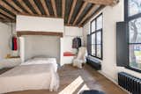 Exposed ceiling beams and wooden floors continue into the bedrooms. Steel clothing racks hang above built-in benches with storage underneath.&nbsp;