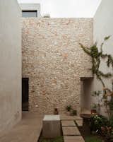 A tall stone-clad wall provides a textured backdrop in the front courtyard. The skull plant pots are by Piedrafuego.
