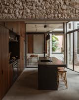 The glassed-in kitchen, which connects to a dry garden in the center of the home, makes use of earthy materials such as parota wood for the millwork, black granite with leather finish for the countertops, and gray cantera stone floors. The pendants are by David Pompa, while the refrigerator is from Whirlpool and the dishwasher from LG.