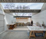 A lofted drawing studio features a sawtooth roof with expansive skylights that frame the branches of a jacaranda tree overhead.