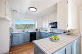 A large picture window in the kitchen offers spectacular views of the surrounding landscape. Blue-painted cabinets add a pop of color below the white tile countertops.