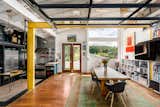 The main dwelling features a colorful, industrial aesthetic offset by white-painted walls and ceilings, as well as warm, wooden details and floors. Yellow steel beams frame the dining room near the open kitchen, which blends a darker palette with stainless-steel appliances.