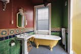The rich color palette extends throughout the home into one of the bathrooms, where red- and green-painted walls complement patterned mosaics that also incorporate yellow and blue accents mirrored in the tile floors and clawfoot tub.