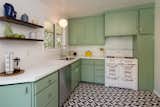 The kitchen, which is filled with playful mint tones, has a view into the backyard and features a patterned tile floor.&nbsp;
