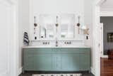 Light teal cabinetry props up a double marble sink, with an old-school mirror sitting neatly above.
