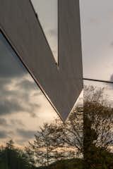 Panes of glass coincide with concrete at oblique angles, reflecting the trees that surround the house.